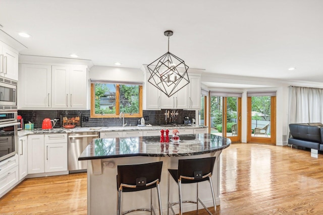 kitchen featuring a center island, light hardwood / wood-style floors, decorative light fixtures, white cabinets, and appliances with stainless steel finishes