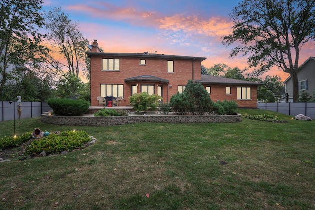 back house at dusk featuring a patio area and a lawn