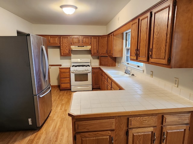 kitchen with tile countertops, sink, white gas range oven, light wood-type flooring, and stainless steel refrigerator