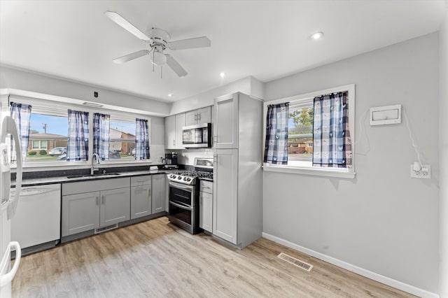 kitchen with gray cabinetry, ceiling fan, sink, stainless steel appliances, and light wood-type flooring