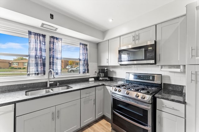 kitchen featuring tasteful backsplash, stainless steel appliances, sink, dark stone countertops, and gray cabinets