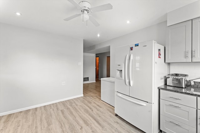 kitchen with decorative backsplash, light wood-type flooring, dark stone counters, ceiling fan, and white refrigerator with ice dispenser