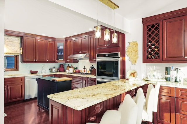 kitchen with appliances with stainless steel finishes, a kitchen bar, kitchen peninsula, hanging light fixtures, and dark wood-type flooring