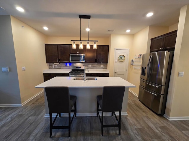 kitchen featuring appliances with stainless steel finishes, dark hardwood / wood-style flooring, a kitchen island with sink, sink, and decorative light fixtures