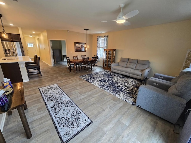 living room featuring ceiling fan, sink, and light wood-type flooring