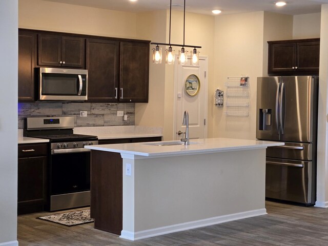 kitchen featuring appliances with stainless steel finishes, tasteful backsplash, sink, pendant lighting, and an island with sink