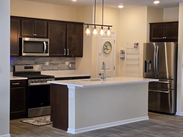 kitchen with pendant lighting, backsplash, stainless steel appliances, dark hardwood / wood-style floors, and a center island with sink