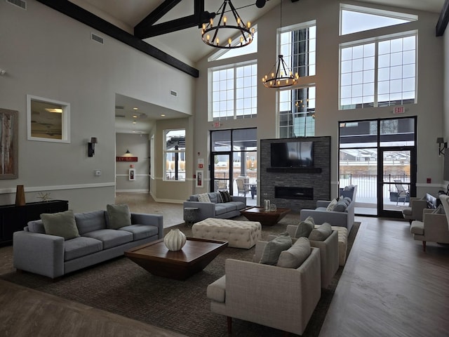 living room with an inviting chandelier, vaulted ceiling with beams, a stone fireplace, and dark hardwood / wood-style flooring