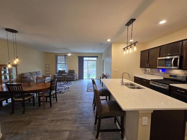 kitchen featuring sink, a kitchen island with sink, stainless steel appliances, dark brown cabinetry, and a kitchen bar