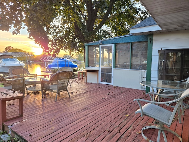 deck at dusk featuring a water view and a sunroom