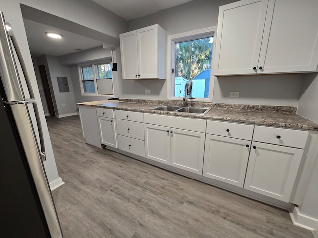 kitchen with white cabinetry, sink, light wood-type flooring, and stainless steel fridge