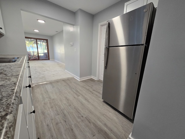 kitchen featuring light stone countertops, sink, white cabinetry, stainless steel refrigerator, and light hardwood / wood-style flooring