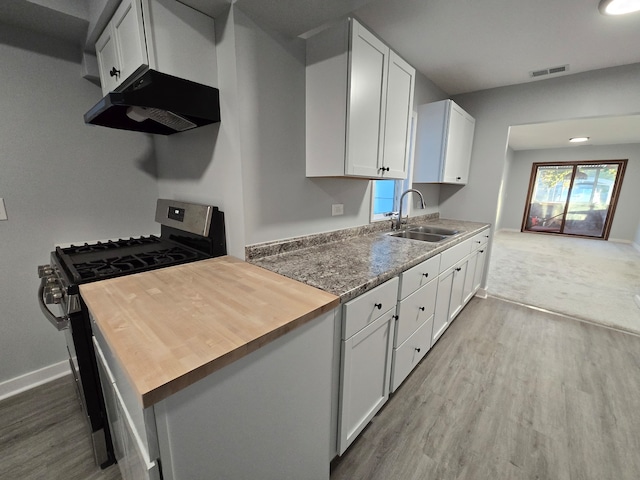 kitchen featuring white cabinetry, light stone countertops, light wood-type flooring, gas range, and sink