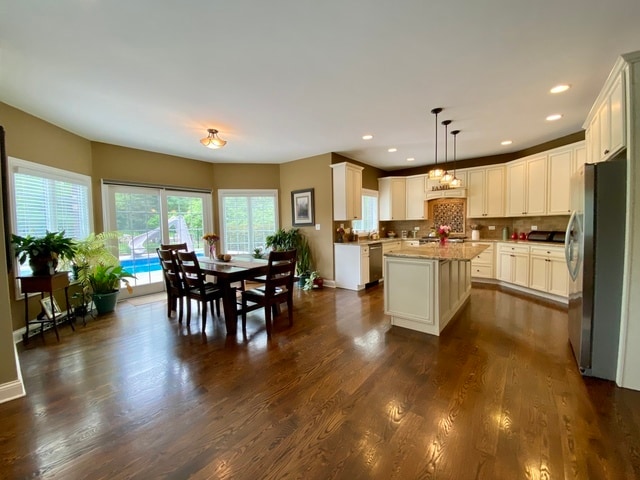 kitchen with appliances with stainless steel finishes, dark hardwood / wood-style flooring, pendant lighting, light stone countertops, and a center island