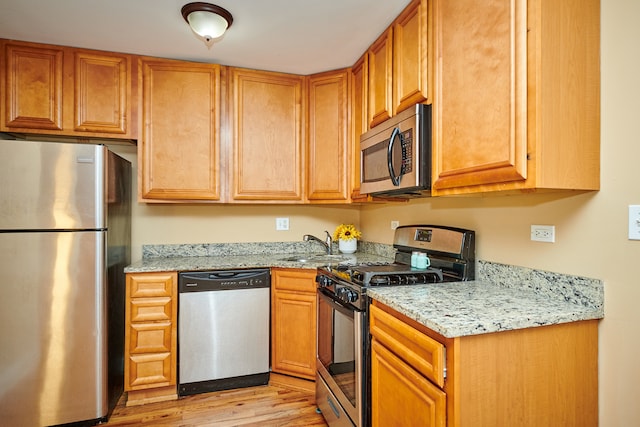 kitchen with sink, appliances with stainless steel finishes, light stone counters, and light wood-type flooring