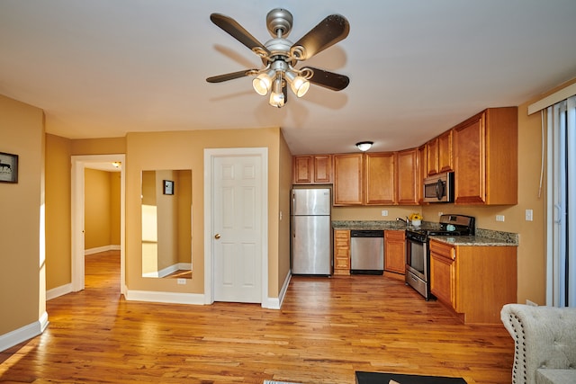 kitchen featuring stone counters, light hardwood / wood-style floors, stainless steel appliances, and ceiling fan