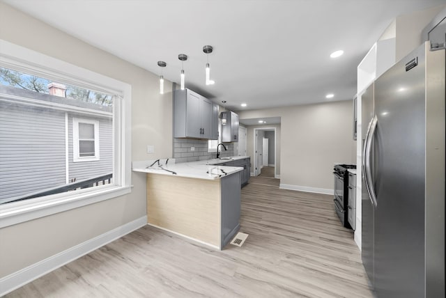 kitchen with kitchen peninsula, stainless steel fridge, hanging light fixtures, light hardwood / wood-style flooring, and black gas range oven