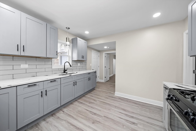 kitchen featuring hanging light fixtures, light wood-type flooring, gas range oven, gray cabinets, and light stone counters