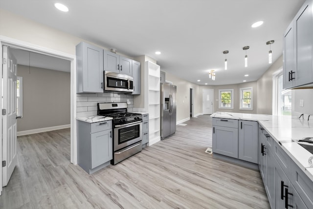 kitchen with appliances with stainless steel finishes, light hardwood / wood-style flooring, light stone counters, and gray cabinets