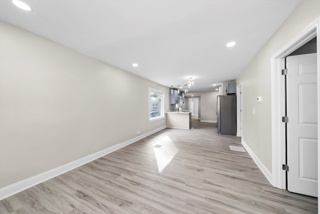 unfurnished living room with light hardwood / wood-style floors, sink, and a chandelier