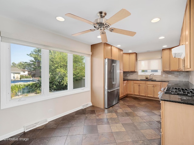 kitchen featuring backsplash, light brown cabinetry, dark stone counters, stainless steel refrigerator, and sink