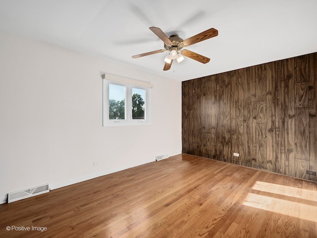 unfurnished room with wood walls, hardwood / wood-style floors, and ceiling fan