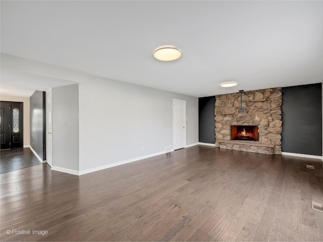 unfurnished living room featuring dark wood-type flooring and a stone fireplace