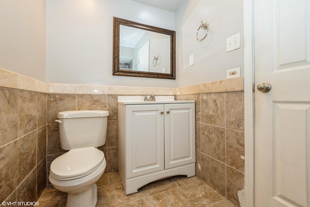 bathroom featuring vanity, toilet, and tile walls