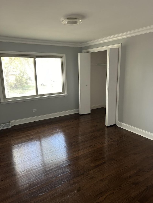 unfurnished bedroom with dark wood-type flooring, ornamental molding, and a closet