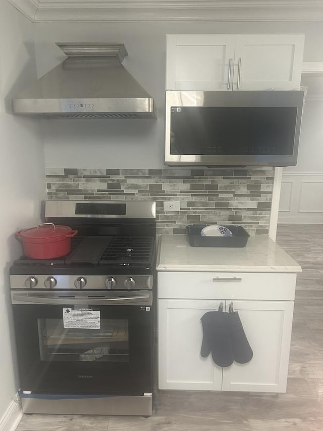 kitchen featuring tasteful backsplash, stainless steel range with gas stovetop, white cabinets, and wall chimney exhaust hood