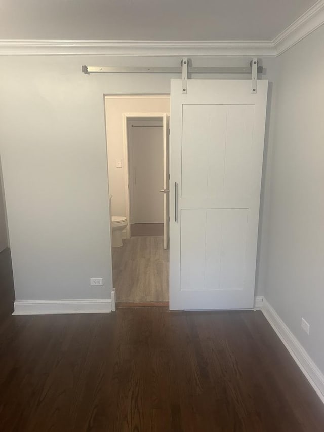 interior space featuring dark hardwood / wood-style flooring, ornamental molding, and a barn door