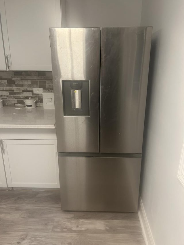 details featuring stainless steel refrigerator with ice dispenser, white cabinets, backsplash, and light hardwood / wood-style floors