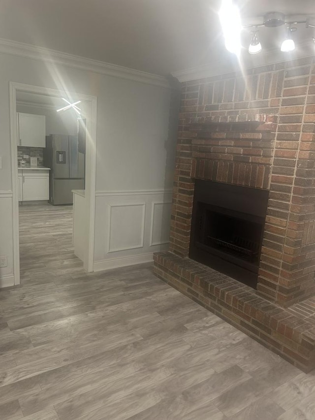 unfurnished living room featuring ornamental molding, a brick fireplace, and light hardwood / wood-style floors