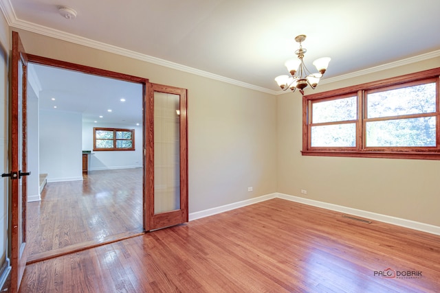 spare room with a wealth of natural light, crown molding, hardwood / wood-style flooring, and an inviting chandelier