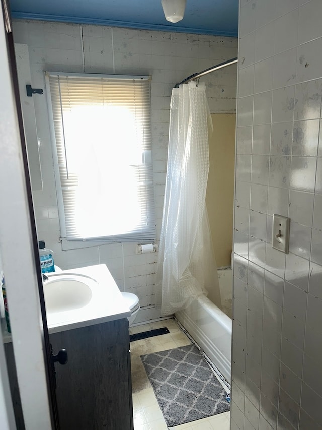 full bathroom featuring tile walls, shower / bath combo with shower curtain, toilet, vanity, and tile patterned floors