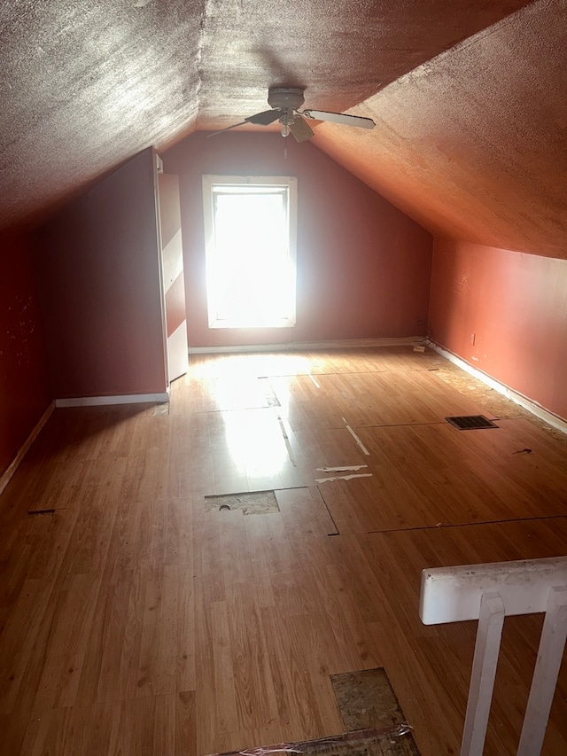 bonus room featuring light hardwood / wood-style flooring, a textured ceiling, vaulted ceiling, and ceiling fan