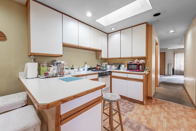 kitchen featuring white range with gas cooktop, a kitchen breakfast bar, white cabinets, and kitchen peninsula