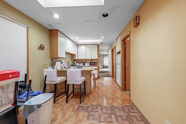 kitchen featuring kitchen peninsula, white cabinetry, a kitchen bar, light wood-type flooring, and white fridge