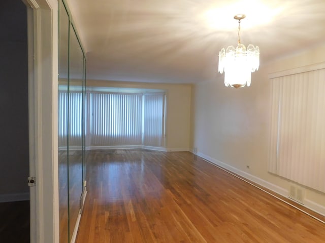 unfurnished room with a notable chandelier and dark hardwood / wood-style floors