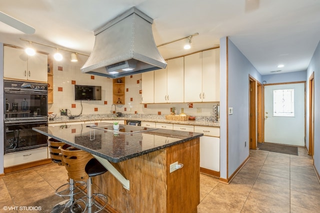 kitchen with island range hood, double oven, a kitchen island, rail lighting, and stone counters