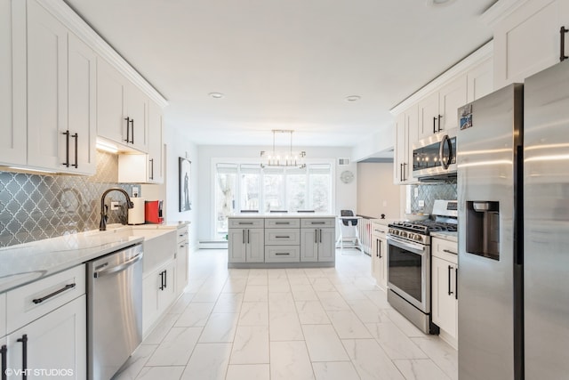 kitchen with light stone countertops, hanging light fixtures, appliances with stainless steel finishes, and white cabinets