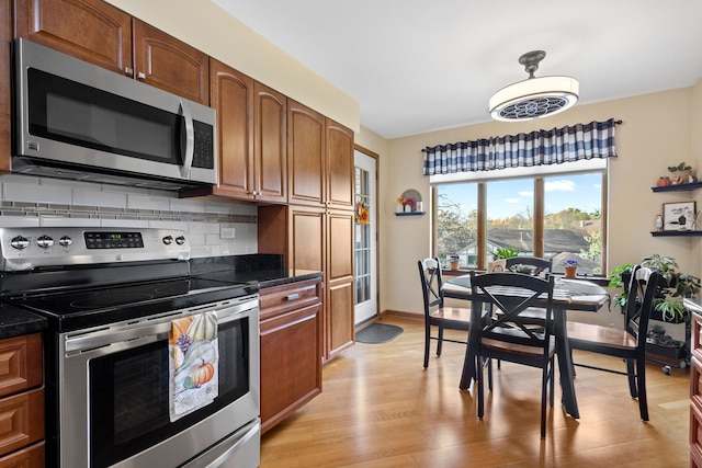 kitchen with light hardwood / wood-style floors, stainless steel appliances, dark stone counters, and backsplash