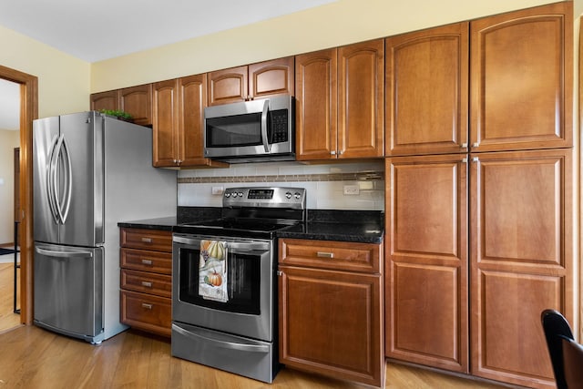 kitchen featuring appliances with stainless steel finishes, tasteful backsplash, light wood-type flooring, and dark stone countertops