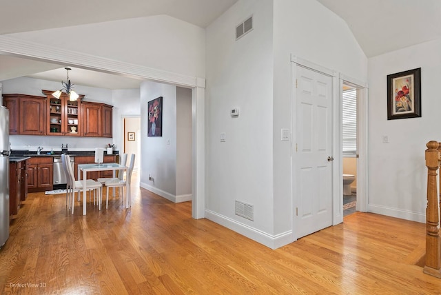 interior space featuring light hardwood / wood-style floors, stainless steel dishwasher, decorative light fixtures, and vaulted ceiling