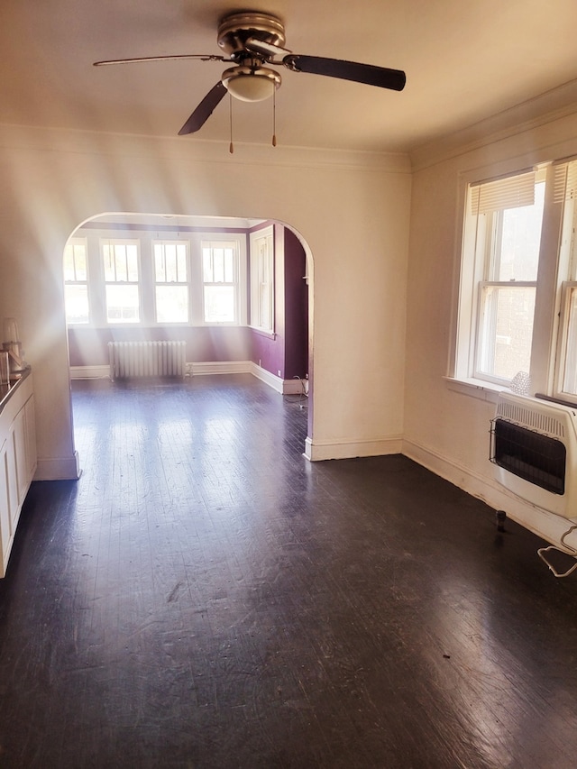 empty room featuring radiator, ceiling fan, heating unit, dark wood-type flooring, and crown molding