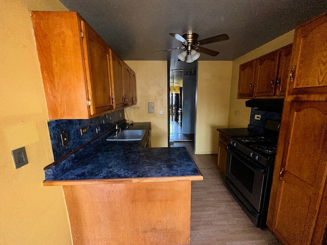 kitchen featuring dark wood-type flooring, kitchen peninsula, ventilation hood, sink, and black gas range oven