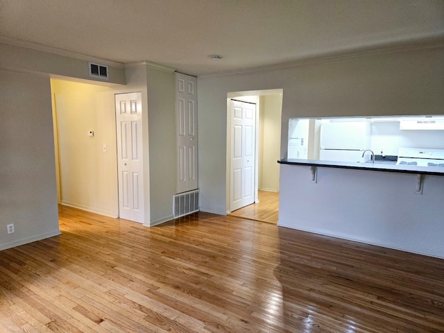 unfurnished living room featuring ornamental molding, sink, and light hardwood / wood-style flooring