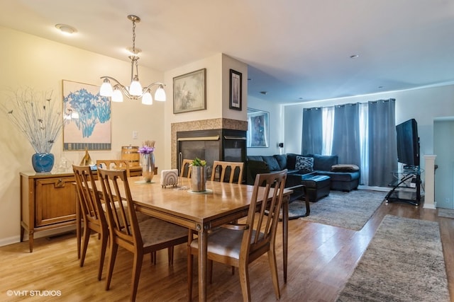 dining area with a multi sided fireplace, hardwood / wood-style floors, and a notable chandelier