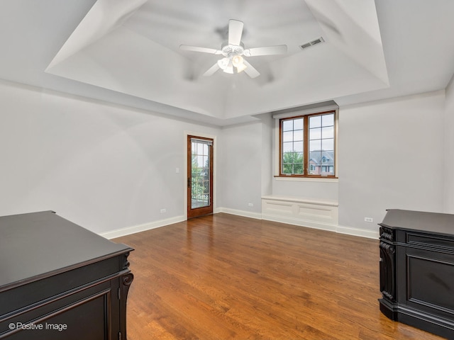 living room with a raised ceiling, wood-type flooring, and ceiling fan