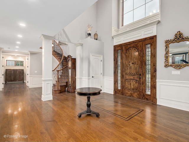 entrance foyer with decorative columns, a towering ceiling, and dark hardwood / wood-style flooring